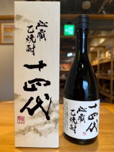 Bottle of sake beside its white textured gift box with black Japanese calligraphy