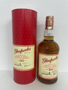 Bottle of Glenfarclas Highland Single Malt Scotch Whisky (10 years) beside red cylindrical gift tube with Glenfarclas branding.