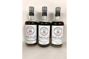 Three bottles of whiskey with white labels reading 26 years lined up on a neutral surface
