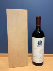 Opus One 2003 red wine bottle beside a tall light wood block on a wooden surface