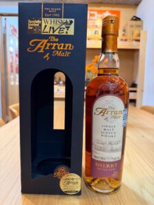 Bottle of The Arran Malt Sherry single malt Scotch whisky standing next to its dark blue presentation box on a wooden table label visible on the bottle