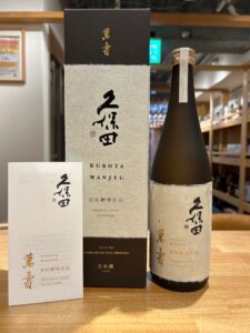 Bottle ofKubota Manjuu sake with beige textured packaging and black box Japanese characters visible on labels