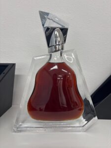 Crystal perfume bottle with red liquid displayed in a clear stand against a white wall