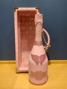 Pink perfume bottle with butterfly wings on the base paired with a tall pink case next to it on a wooden surface