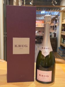 Bottle of Krug Rosé champagne next to a tall purple Krug box on a wooden table in a store It shows KRUG ROSÉ on the label and box