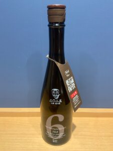 Dark glass bottle with brown flip top cap and a hanging tag labeled No6 on a wooden table against a blue wall