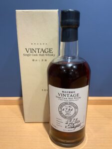 Bottle of Vintage Single Cask Malt Whisky with a plain beige box behind on a wooden surface