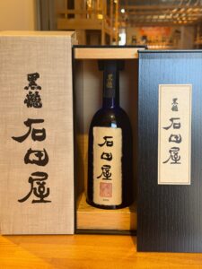 Bottle of sake in a wooden display box with Japanese label flanked by textured gift boxes year 2023 visible on the label