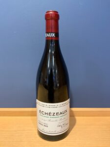 Bottle of red wine with a red capsule against a blue wall label reads Échezeaux vintage 2022
