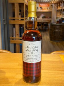 Bottle of blended malt Scotch whisky with a gold cap on a wooden table blurred shop shelves in the background