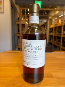 Bottle of Nikka whisky, label reading 'NIKKA SINGLE CASK MALT WHISKY 10 YEARS OLD', on a wooden table with blurred store shelves in the background