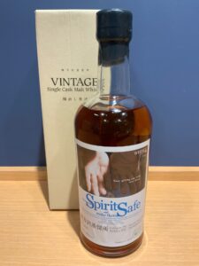 Bottle of Vintage Single Cask Malt Whisky beside its beige packaging on a wooden surface foreground shows the bottle cap