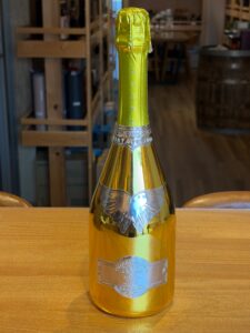 Gold foil wrapped champagne bottle on a wooden table with a blurred shop interior in the background
