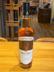 Bottle of Compass Box The Spice Tree whiskey on a wooden table in a shop close up front view with blurred background shelves and barrels behind