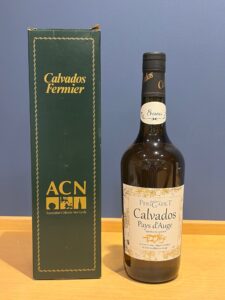 Bottle of Calvados Pays dAuge beside a dark green Calvados Fermier box on a wooden table