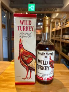 Bottle of Wild Turkey 101 proof bourbon beside its white and red box with a large turkey illustration in a liquor store setting