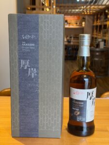 Box of The Akkeshi Single Malt Whisky beside a whisky bottle on a wooden table in a shop setting gray decorative pattern on box and label visible