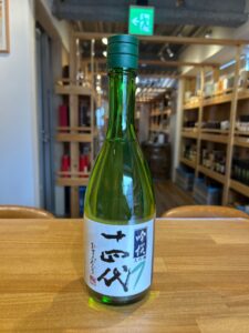 Green glass sake bottle on a wooden counter with a white label featuring Japanese characters inside a shop