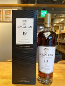 The Macallan 18 year old Highland Single Malt whisky bottle beside its dark patterned box on a wooden surface