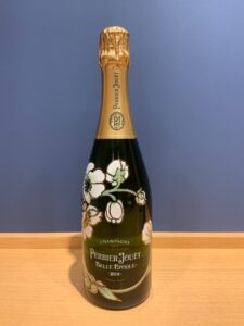 3C22LqIjRnGOg5uBdUzTHLT8m2fNJo0CvKtAl8M3 お酒買取専門店LIQUORJOYリカージョイ Perrier Jouët Belle Époque champagne bottle with gold foil top and white florals on dark green glass 2018 standing on a wooden surface against a blue wall