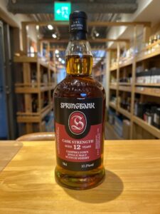 Bottle of Springbank 12 year old cask strength single malt Scotch whisky on a wooden table in a store with shelves of bottles in the background