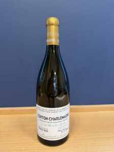 Wine bottle with a gold foil neck on a wooden table blue background label reads Corton Charlemagne