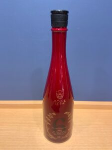 Iodxw7cNjvphHzLCtVD2yOaQc0yUzrB0hFYEIGzL 横浜と東京のお酒買取専門店LIQUORJOYリカージョイ Red glass bottle with black cap on a light wooden table against a blue wall close up of neck and label visible