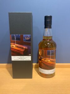 Bottle of whiskey with a black cap next to a dark display box on a wooden surface label visible indicating 700 ml and distillery details