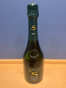 Champagne bottle with a green foil neck and a gold S logo 2015 neck label visible on a wooden surface