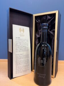 WTueXYHYA21HvX1QMb6sxAC26qIrvpJWTlzWqsr7 お酒買取専門店LIQUORJOYリカージョイ Dark wooden display box with gold trim holds a tall black bottle labeled RANBIKI 2014 on a satin lining plus an informational card nearby