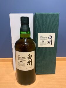 Bottle of The Hakushu 25 Year Old Japanese whisky with green gift box beside it on a wooden surface