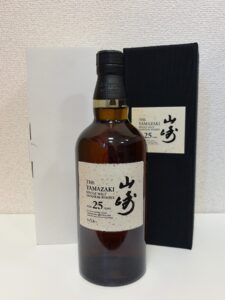 Bottle of The Yamazaki 25 Year Old Single Malt Japanese Whisky with black box in background and white label on beige paper wrapper behind