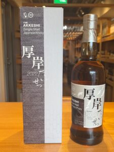 A box labeled The Akkeshi Single Malt Japanese Whisky beside a whisky bottle on a wooden table 2022 edition in a store