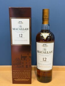 The Macallan 12 year old Highland Single Malt Scotch Whisky bottle next to its burgundy box against a blue background