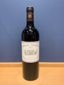 Bottle of Château Margaux 2021 red wine standing upright on a wooden table against a blue wall