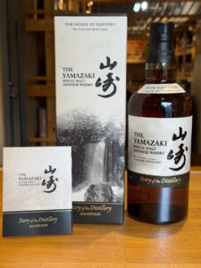 Bottle of The Yamazaki whisky with its white and black boxed packaging and matching cards on a wooden counter