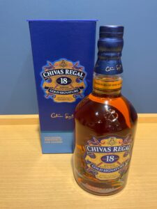 Blue Chivas Regal gift box beside a bottle of Chivas Regal Gold Signature 18 year old whisky on a wooden table