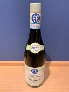 Bottle of Trebbiano dAbruzzo wine with blue EP logo and 2022 production label on a wooden surface against a blue wall