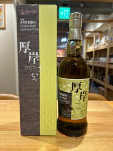 A bottle of The Akkeshi Single Malt Japanese Whisky beside its green and brown decorative box on a wooden table in a store display.