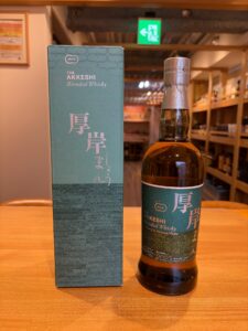Bottle of Akkeshi Blended Whisky next to its teal box on a wooden table in a shop setting.