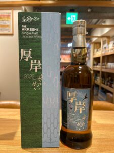 Bottle of The Akkeshi Single Malt Japanese Whisky beside its green and blue patterned box on a wooden table.