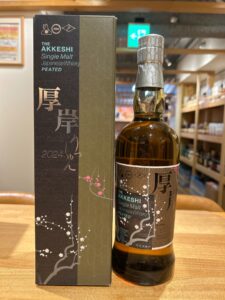 Bottle of The Akkeshi Single Malt Japanese Whisky, Peated, standing beside its branded box with cherry blossom motif on a wooden table.