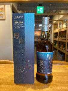 Blue box and bottle of Akkeshi Single Malt Japanese Whisky Peated on a wooden counter/bar area.
