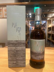 Whisky bottle beside its gray box on a wooden counter, label shows Japanese characters and 2024.