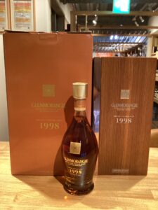 Glenmorangie 1998 Grand Vintage Malt whisky bottle in front of its orange and wood toned boxes on a wooden surface