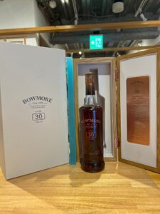 Bottle of Bowmore 30 year old whisky in an open display case with a white outer box and wooden framed doors background shows an exit sign