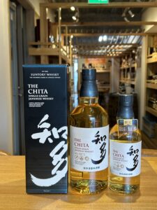 Boxed Suntory Whisky The Chita single grain bottle with two unboxed bottles on a wooden counter in a store display labels visible