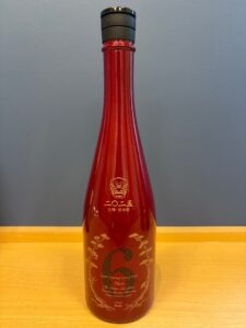 Red glass bottle with a black cap gold decorative label and Asian characters on the front photographed upright on a wooden surface