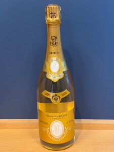 Gold Cristal champagne bottle on a wooden table against a blue wall Louis Roederer Cristal label visible