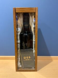 Wooden glass front display case housing a dark bottle labeled Suntory Whisky Blenders Choice surrounded by satin lining
